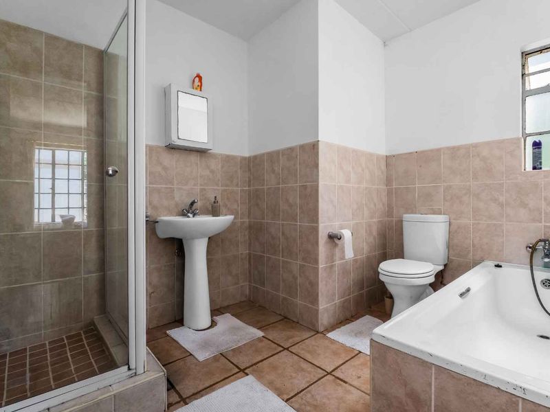 A functional bathroom featuring a pedestal basin, a separate shower enclosure, a bathtub, and tiled finishes throughout.