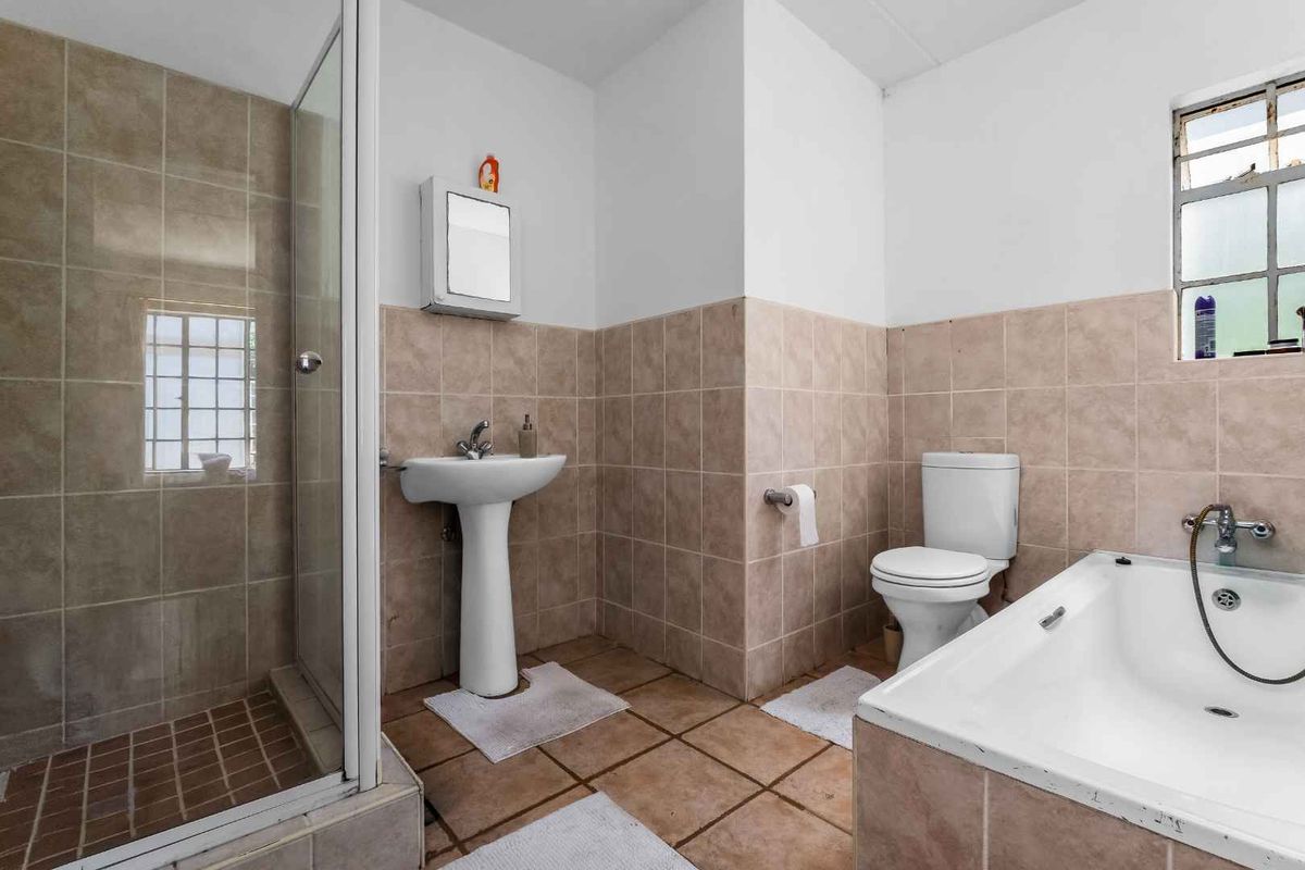 A functional bathroom featuring a pedestal basin, a separate shower enclosure, a bathtub, and tiled finishes throughout.