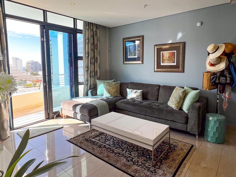 A bright living room featuring large glass sliding doors that open onto a balcony, with polished floor tiles and neutral wall finishes.