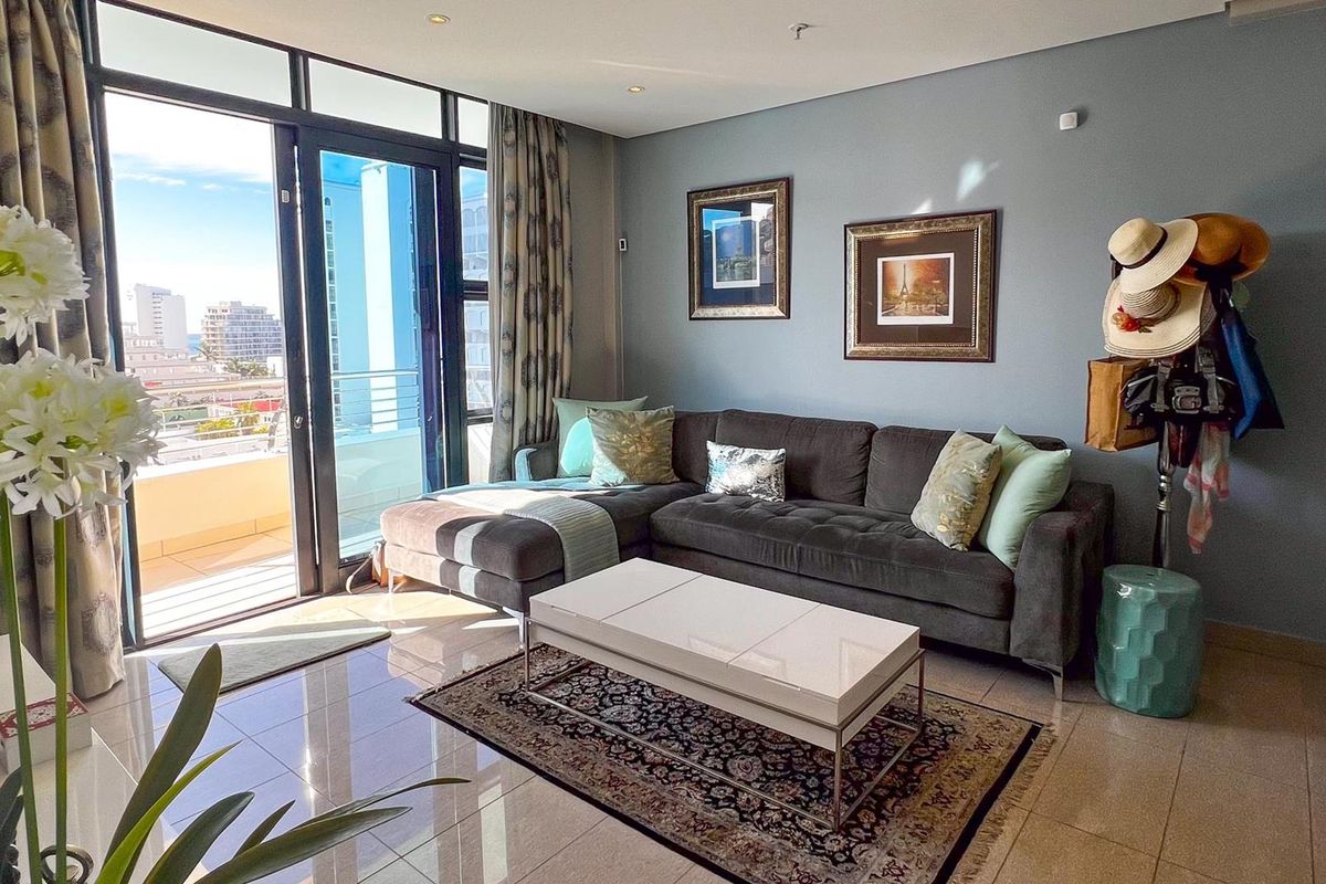 A bright living room featuring large glass sliding doors that open onto a balcony, with polished floor tiles and neutral wall finishes.