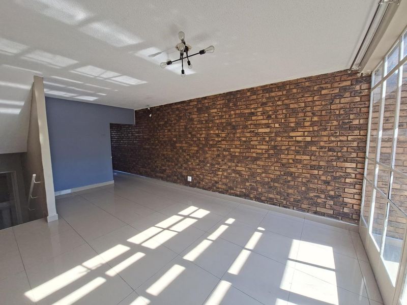 Spacious living area featuring a prominent exposed brick wall, neutral tiled flooring, and natural light from a large glass sliding door.