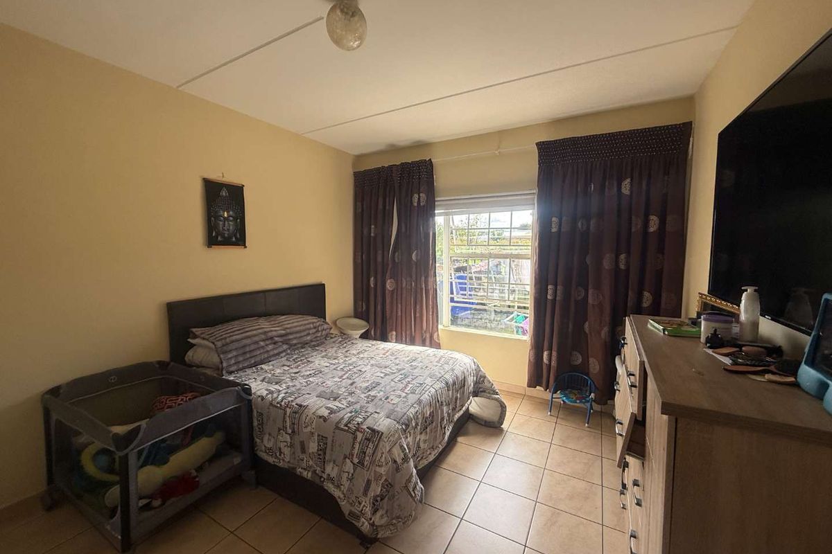 A functional bedroom featuring tiled flooring, a window with curtain treatments, and a standard ceiling light fixture.