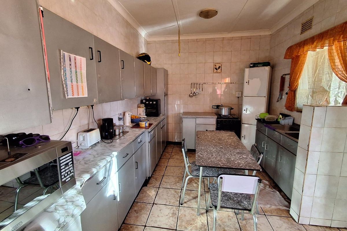 A dated kitchen featuring tiled walls and flooring, laminate countertops, and original built-in cabinetry, offering significant potential for a modern renovation.