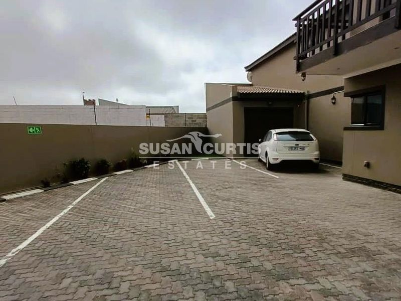 Exterior view of the guest house featuring a paved driveway, garage access, and a balcony on the upper level.