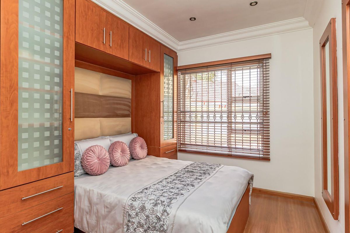 A well-maintained bedroom featuring extensive built-in wooden cabinetry, laminate flooring, recessed lighting, and venetian blinds for privacy.