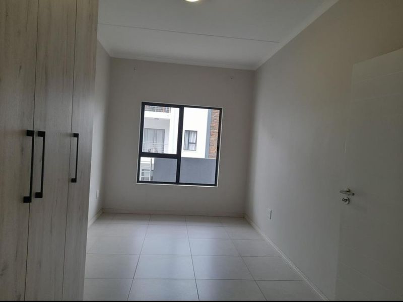A clean, empty bedroom featuring neutral tiled flooring, built-in cupboards, and a modern aluminium window frame.