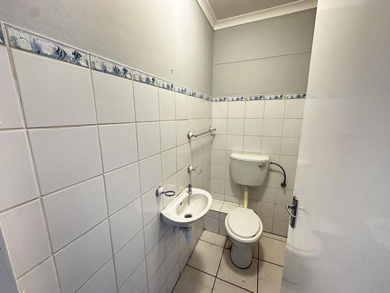 A compact bathroom featuring a wall-mounted basin, standard toilet, and white ceramic wall tiles with a decorative border.