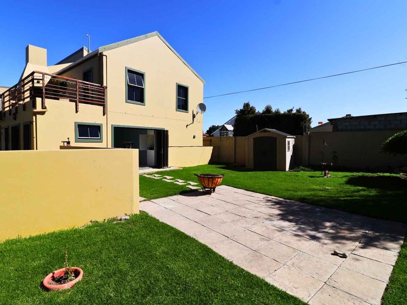 Rear view of the property featuring a paved patio area, a well-maintained lawn, a boundary wall, and an upper-level balcony.