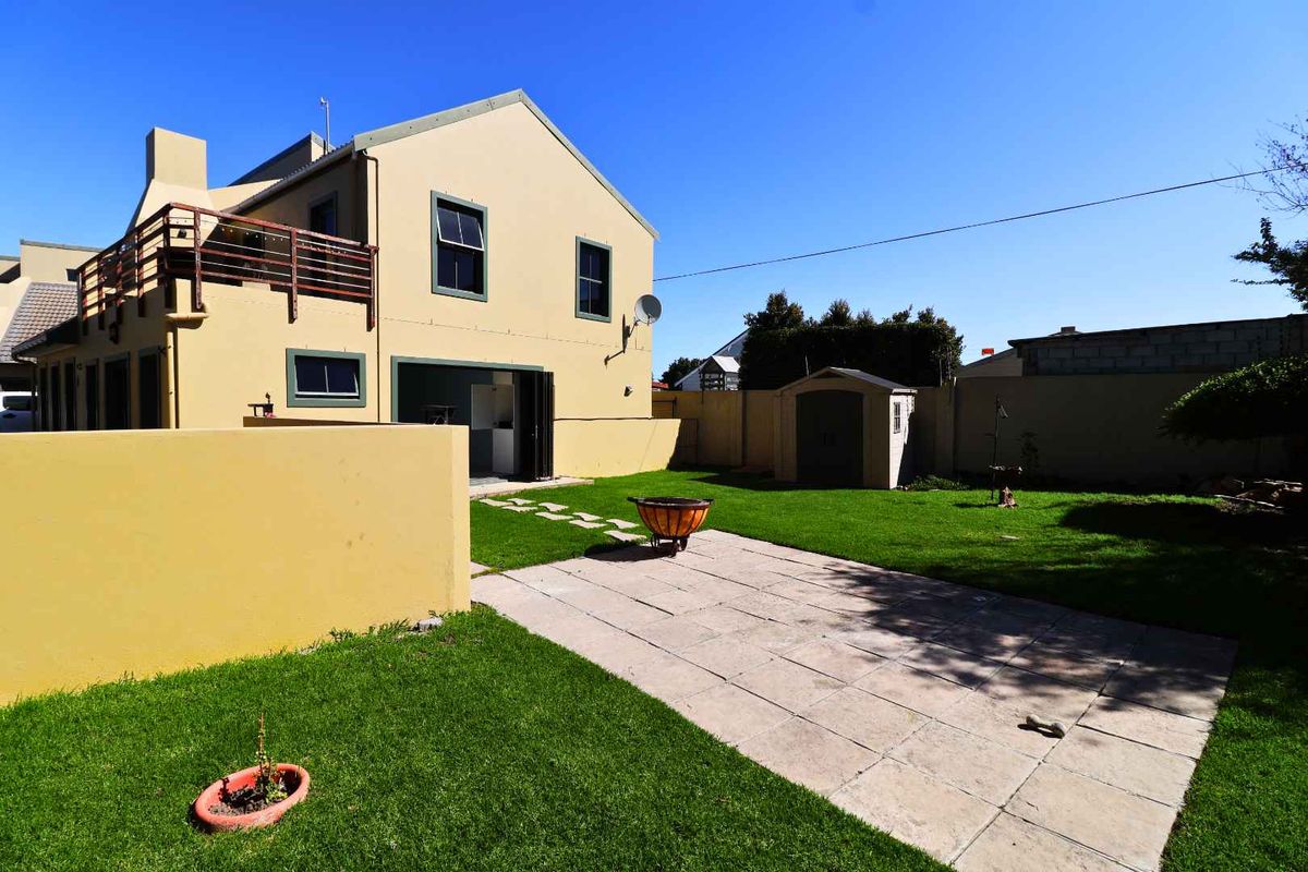 Rear view of the property featuring a paved patio area, a well-maintained lawn, a boundary wall, and an upper-level balcony.