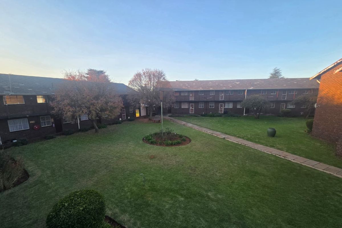 A view of the communal garden and courtyard area between apartment blocks, featuring established trees, lawn, and paved walkways.