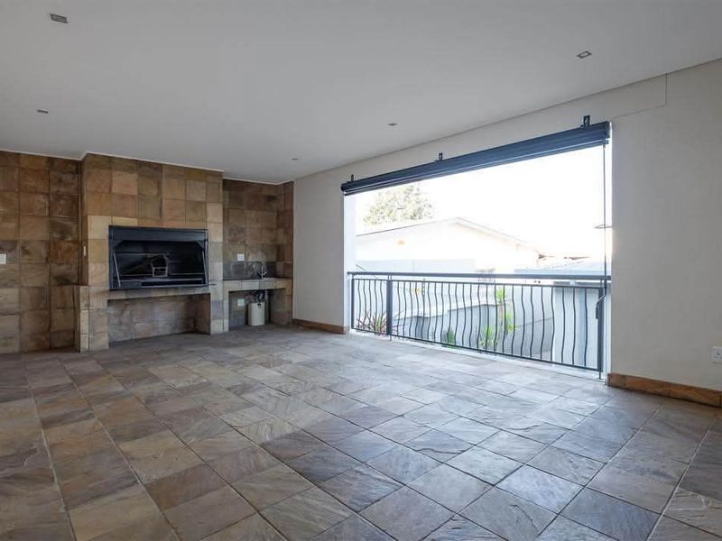 Spacious covered patio featuring stone tile flooring, a built-in braai with stone cladding, and a metal balustrade overlooking the exterior.