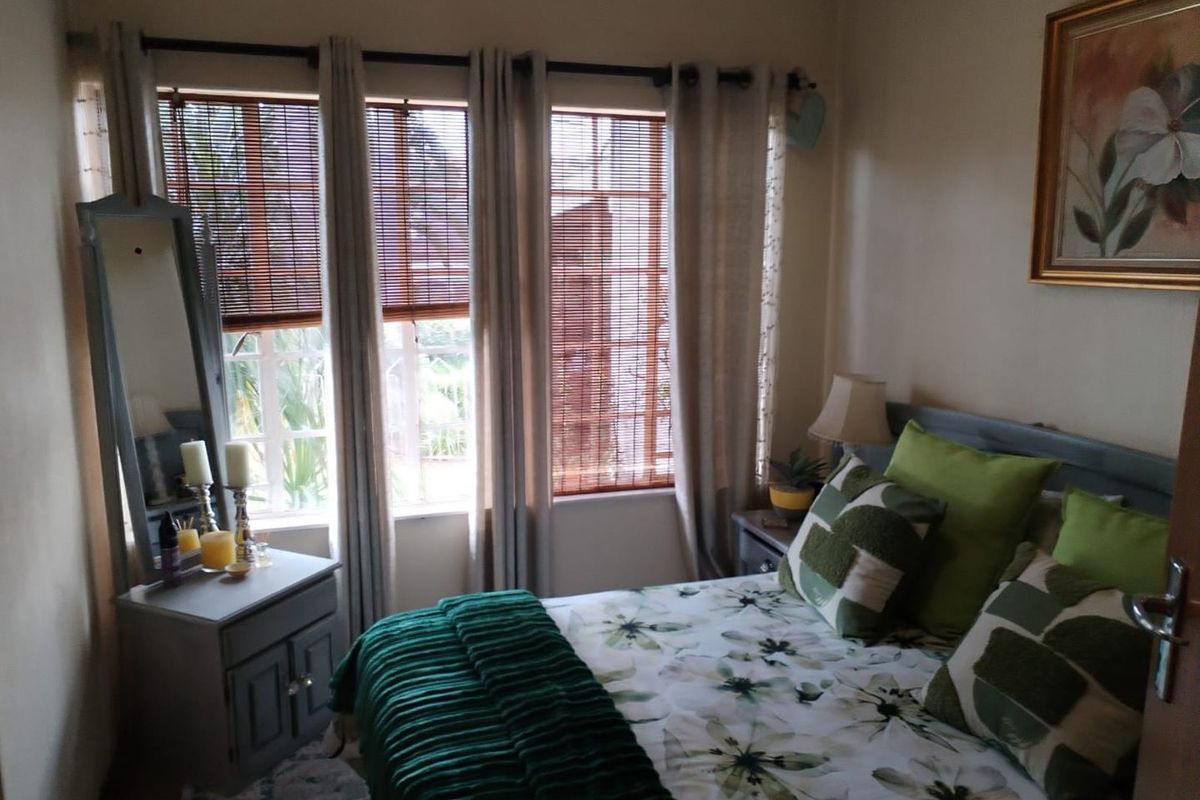A cozy bedroom featuring large windows with integrated blinds, providing natural light and a view of the exterior garden area.