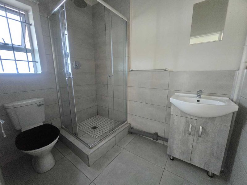 A functional bathroom featuring a glass shower enclosure, a vanity basin, and neutral grey floor-to-ceiling tiling.
