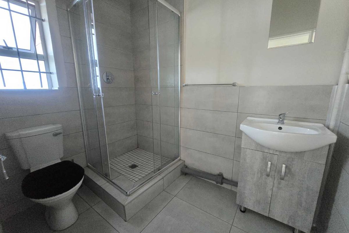 A functional bathroom featuring a glass shower enclosure, a vanity basin, and neutral grey floor-to-ceiling tiling.