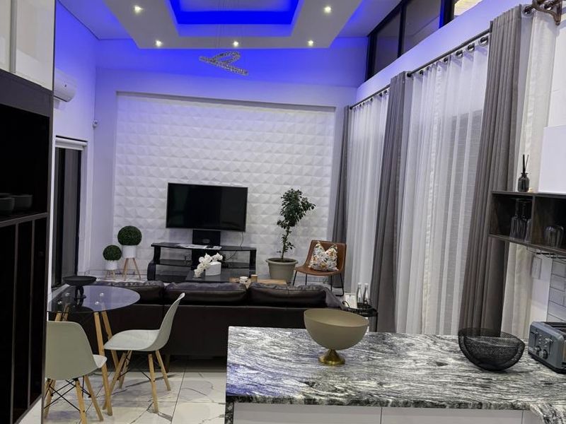 Modern open-plan living and kitchen area featuring high-gloss cabinetry, granite countertops, marble-look flooring, and a striking recessed ceiling with ambient blue lighting.