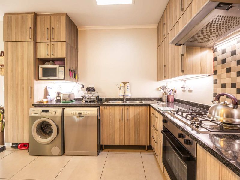 Modern kitchen featuring wood-look cabinetry, granite countertops, integrated appliances, gas hob, and a stylish mosaic tile backsplash.