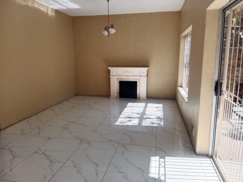 An empty living room featuring large marble-look floor tiles, a decorative fireplace, and a sliding glass door with a security gate leading outdoors.