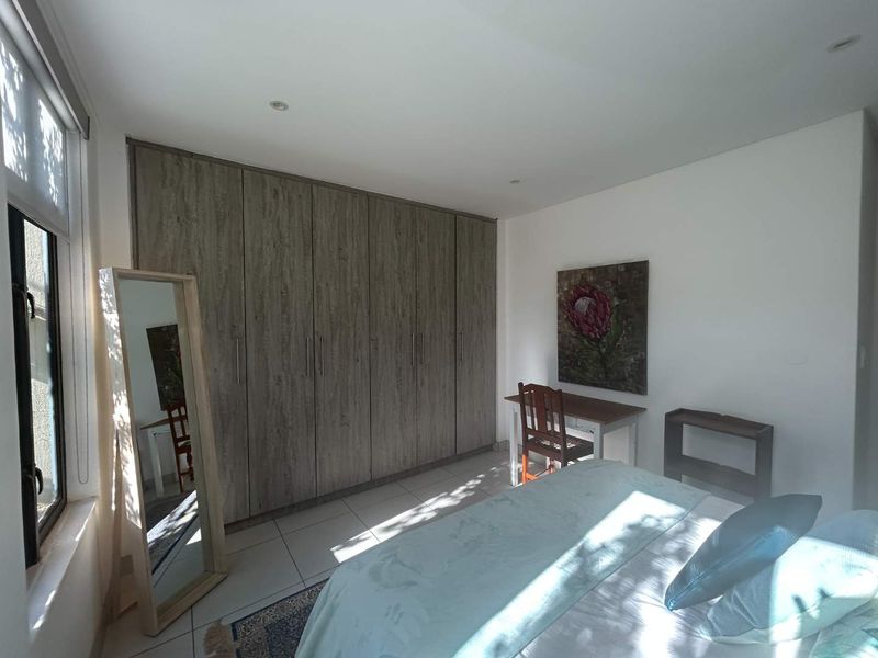 A well-maintained bedroom featuring modern wood-finish built-in cupboards, neutral tiled flooring, and recessed lighting, offering a clean and functional living space.