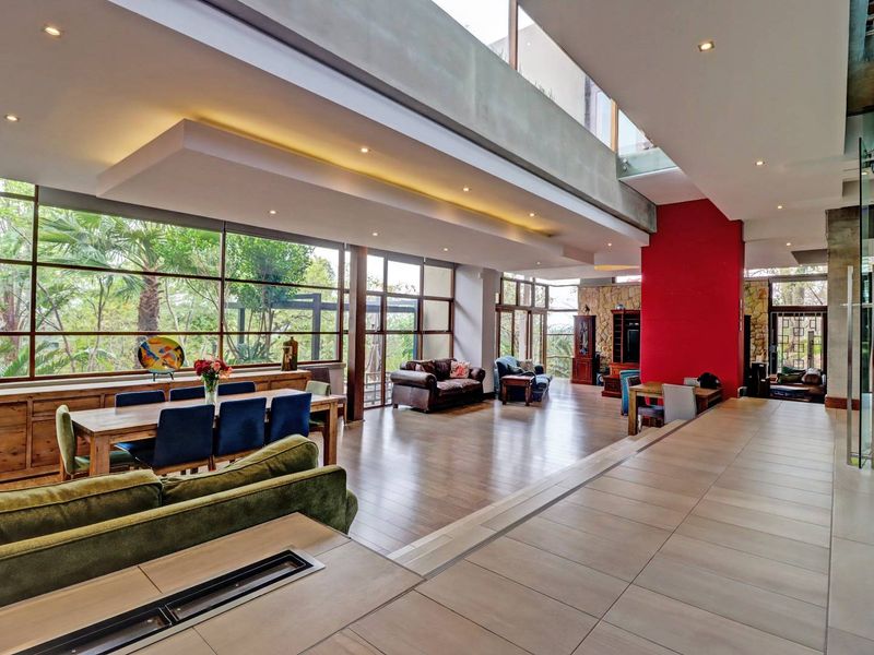 Spacious open-plan living and dining area featuring double volume ceilings, large glass windows, and a striking stone feature wall with modern tiled and laminate flooring.