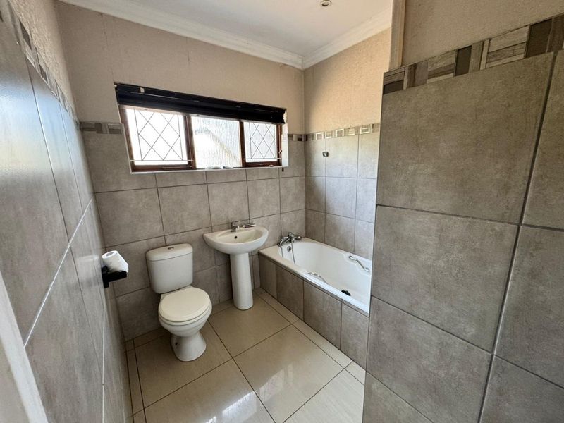 A functional bathroom featuring a pedestal basin, toilet, and built-in bathtub with neutral ceramic tiling throughout.