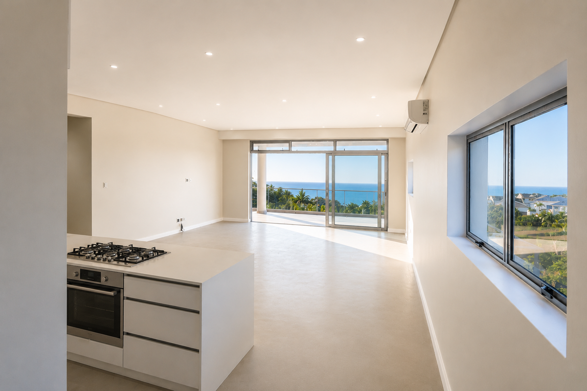 Spacious open-plan living area featuring a modern kitchen island with built-in oven and hob, leading to a balcony with scenic ocean views.