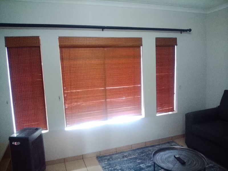 A living room area featuring tiled flooring, cove cornicing, and three windows fitted with bamboo blinds and a curtain rod.