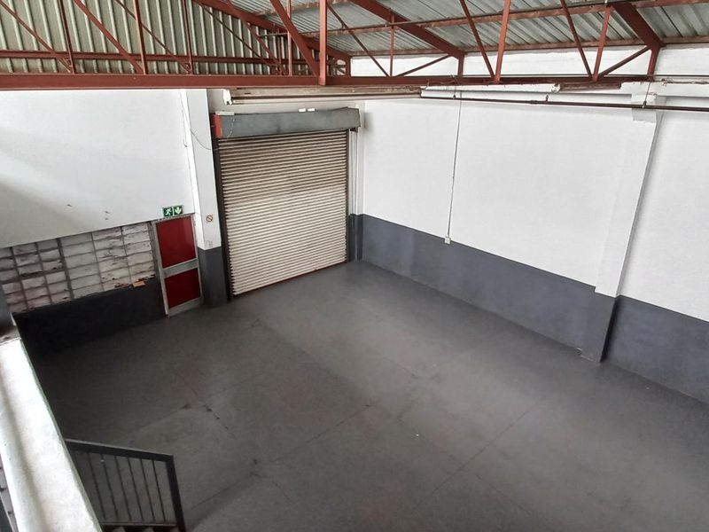 Spacious industrial warehouse unit featuring high ceilings with exposed steel trusses, a large roller shutter door, and durable painted concrete flooring.
