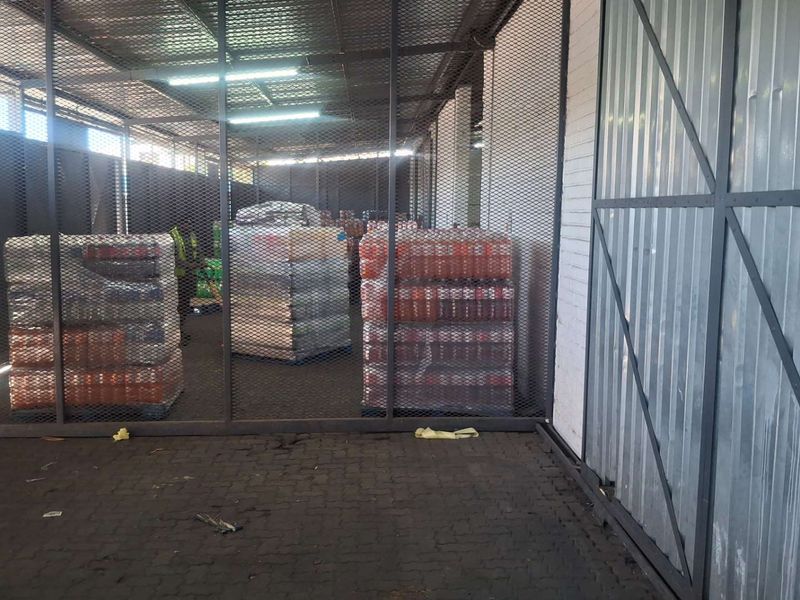A secure industrial utility or storage area featuring metal mesh partitioning, corrugated wall cladding, and durable paved flooring with overhead fluorescent lighting.