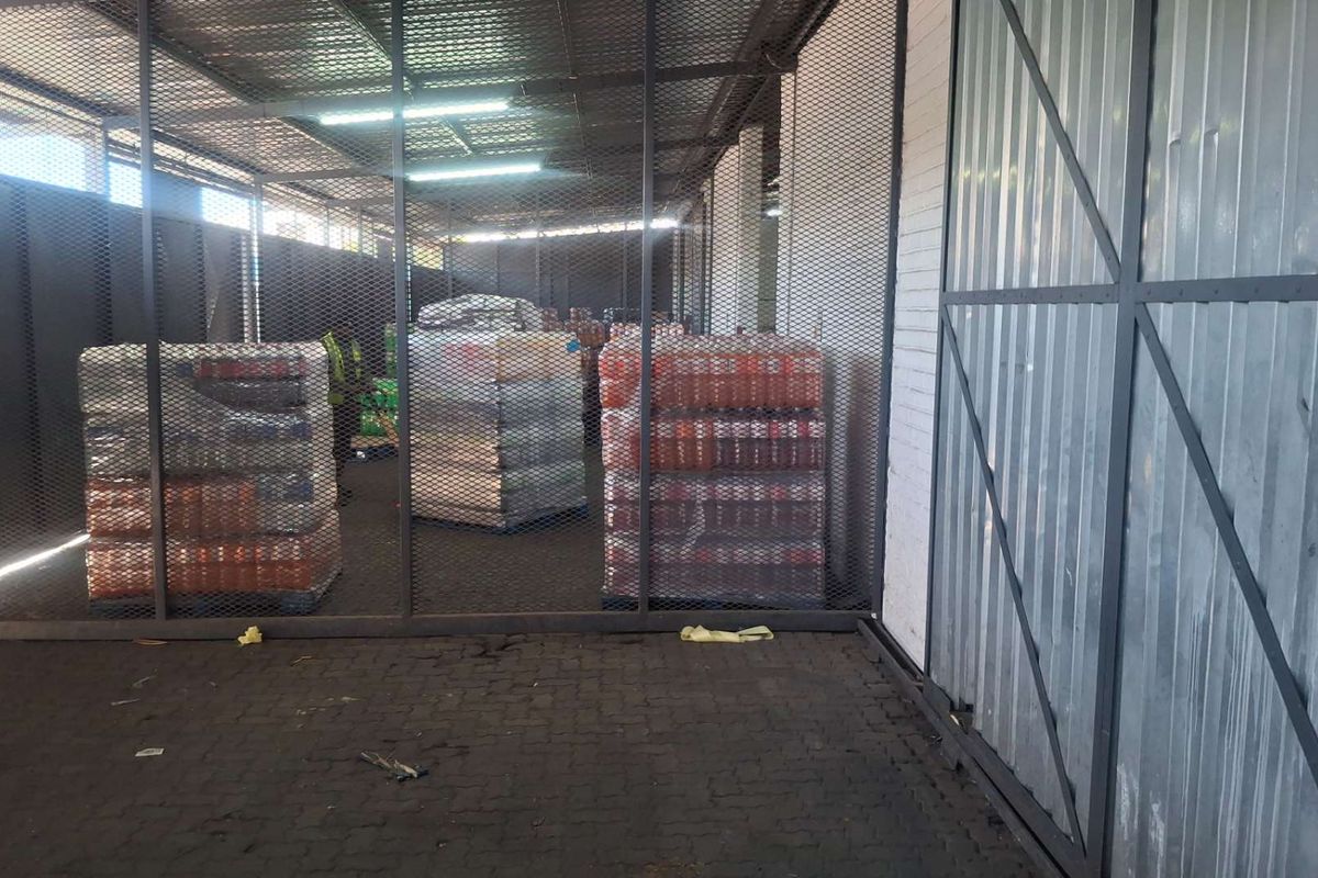 A secure industrial utility or storage area featuring metal mesh partitioning, corrugated wall cladding, and durable paved flooring with overhead fluorescent lighting.