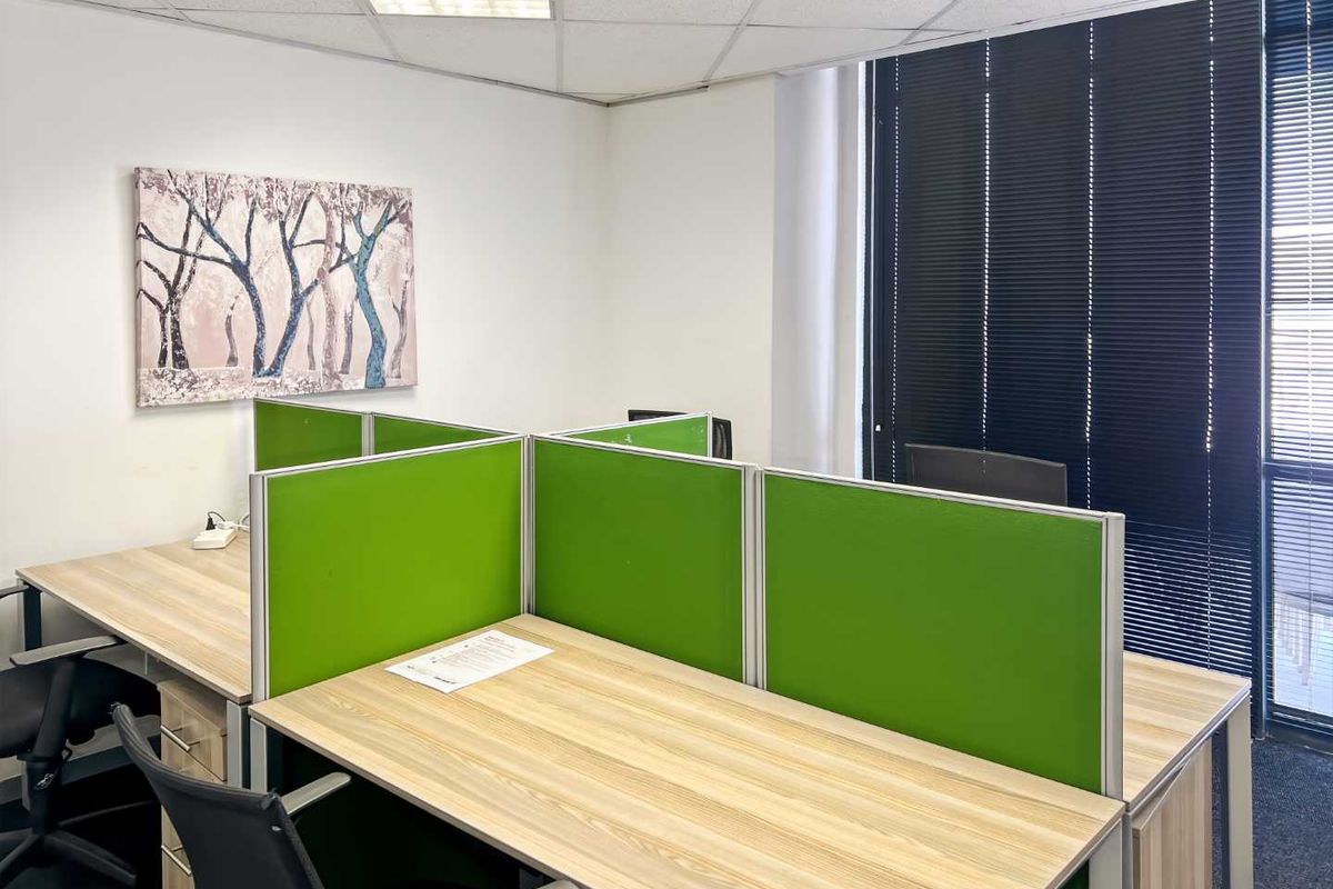 A functional office space featuring built-in workstation partitions, suspended ceiling tiles, and large windows with venetian blinds for natural light control.
