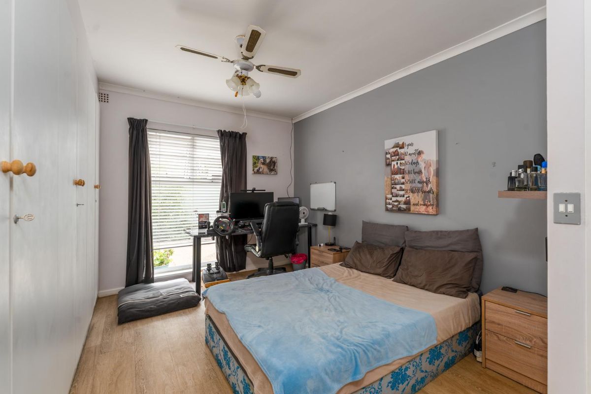 A functional bedroom featuring light wood-look flooring, built-in wardrobe storage, and a ceiling fan, offering a comfortable and practical living space.