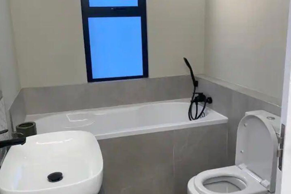 Modern bathroom featuring a built-in bathtub, contemporary vessel sink, and a toilet with sleek black fixtures and neutral wall tiling.