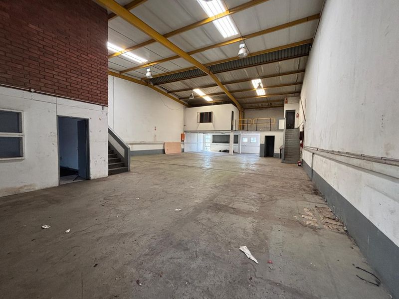 Spacious industrial warehouse unit featuring high ceilings with exposed steel trusses, concrete flooring, and a mezzanine level suitable for storage or office conversion.