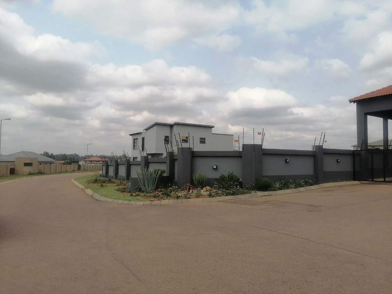 Street view of a residential property featuring a modern perimeter wall with electric fencing and landscaped garden beds.