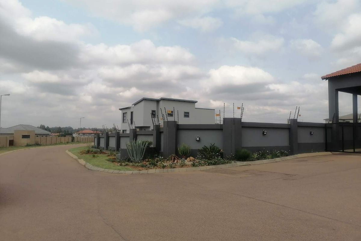 Street view of a residential property featuring a modern perimeter wall with electric fencing and landscaped garden beds.