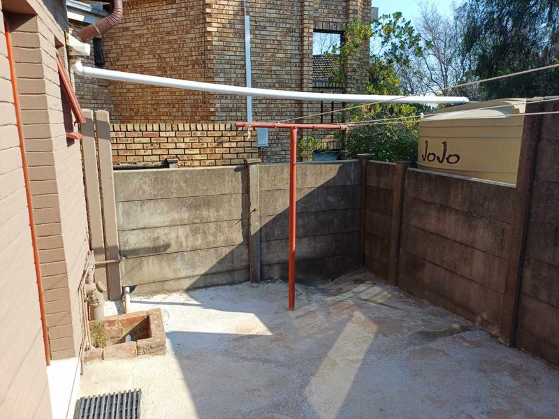 A rear exterior utility area featuring a concrete boundary wall, drainage system, and a water storage tank.