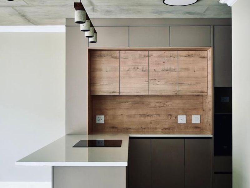 Modern kitchen featuring sleek cabinetry, wood-look accents, stone countertops, integrated hob, and an exposed concrete ceiling in a contemporary open-plan layout.