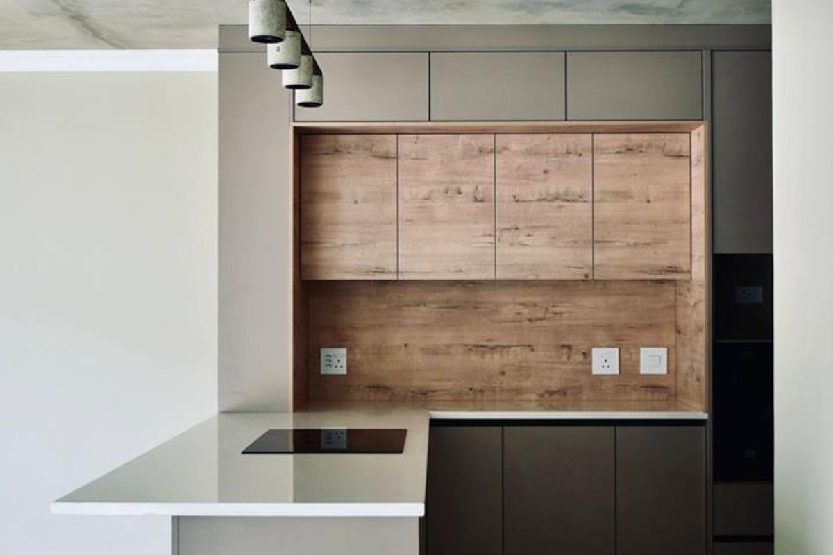 Modern kitchen featuring sleek cabinetry, wood-look accents, stone countertops, integrated hob, and an exposed concrete ceiling in a contemporary open-plan layout.
