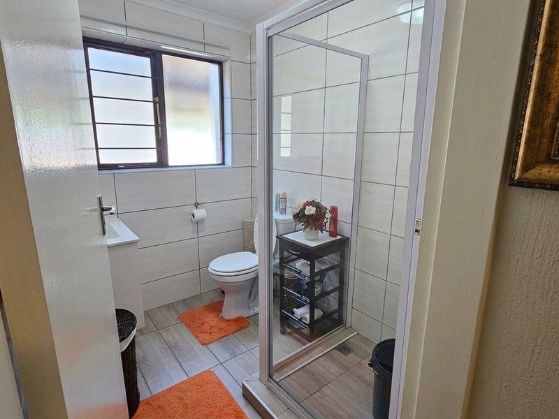 A functional bathroom featuring a shower enclosure, toilet, and vanity basin with neutral wall and floor tiling.