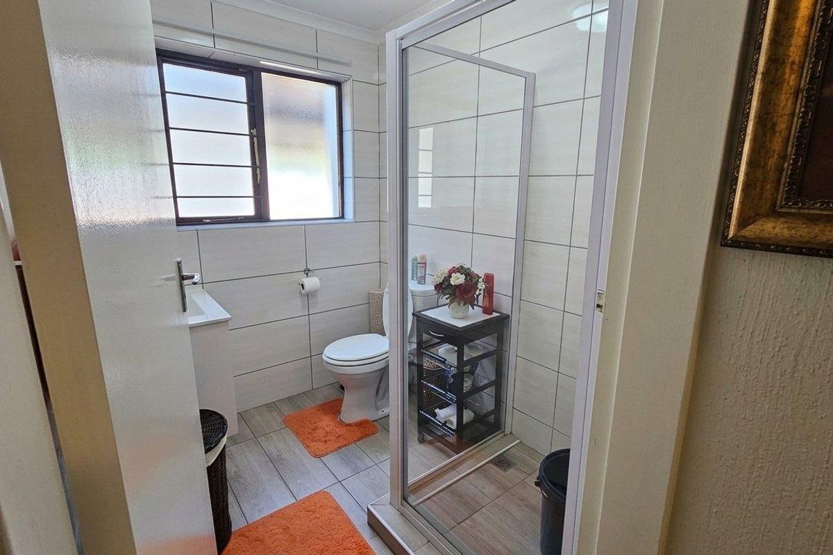 A functional bathroom featuring a shower enclosure, toilet, and vanity basin with neutral wall and floor tiling.