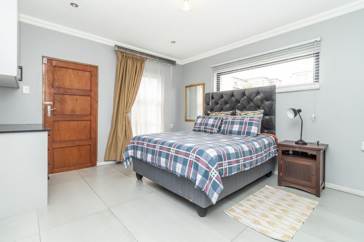 A well-maintained bedroom featuring neutral grey walls, large format floor tiles, recessed ceiling lighting, and a solid timber door.
