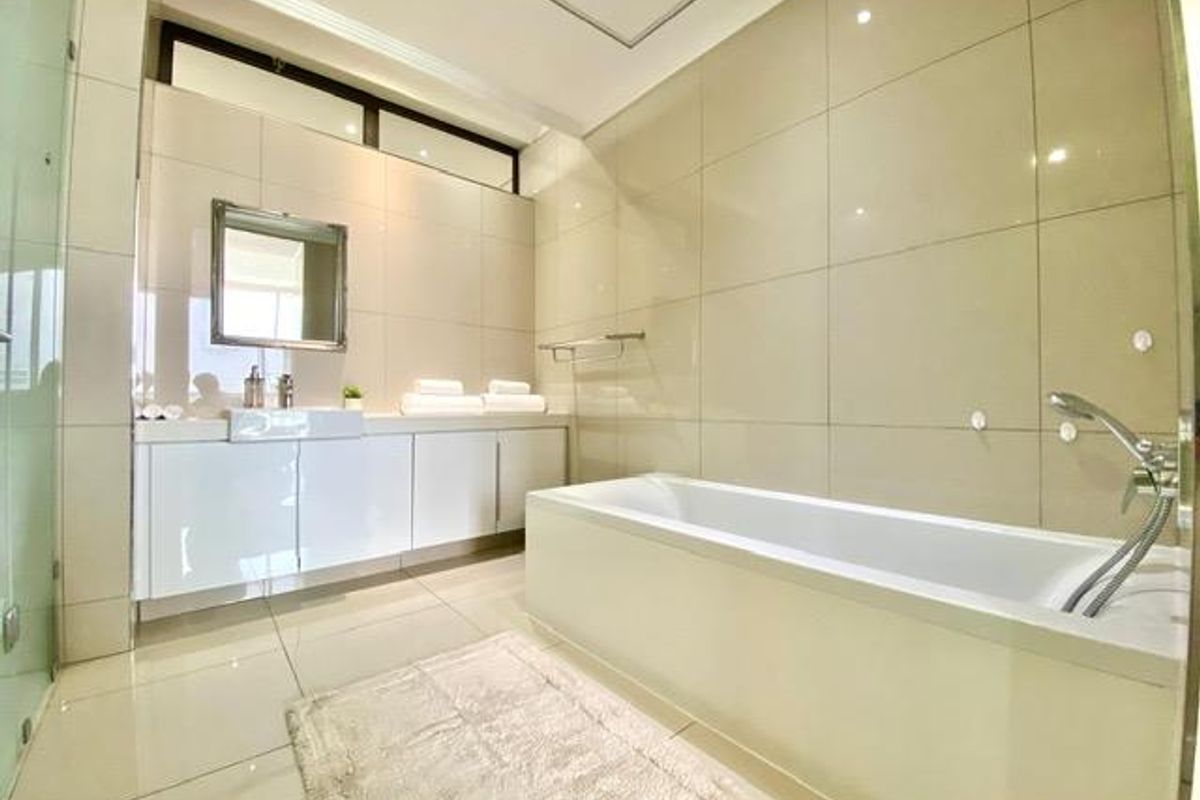 Modern bathroom featuring a white bathtub, wall-mounted vanity with integrated basin, and floor-to-ceiling neutral wall tiles.