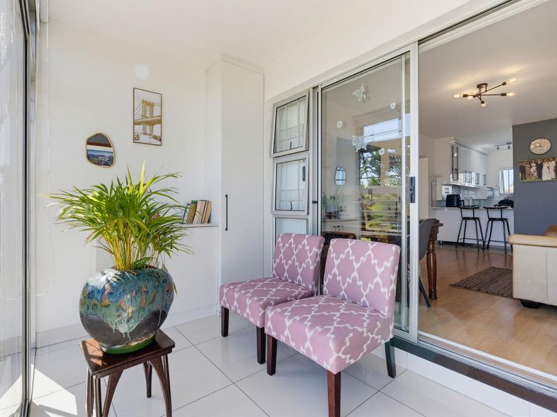 A bright, enclosed balcony or sunroom featuring tiled flooring, built-in storage, and sliding glass doors providing a seamless transition to the open-plan living area.