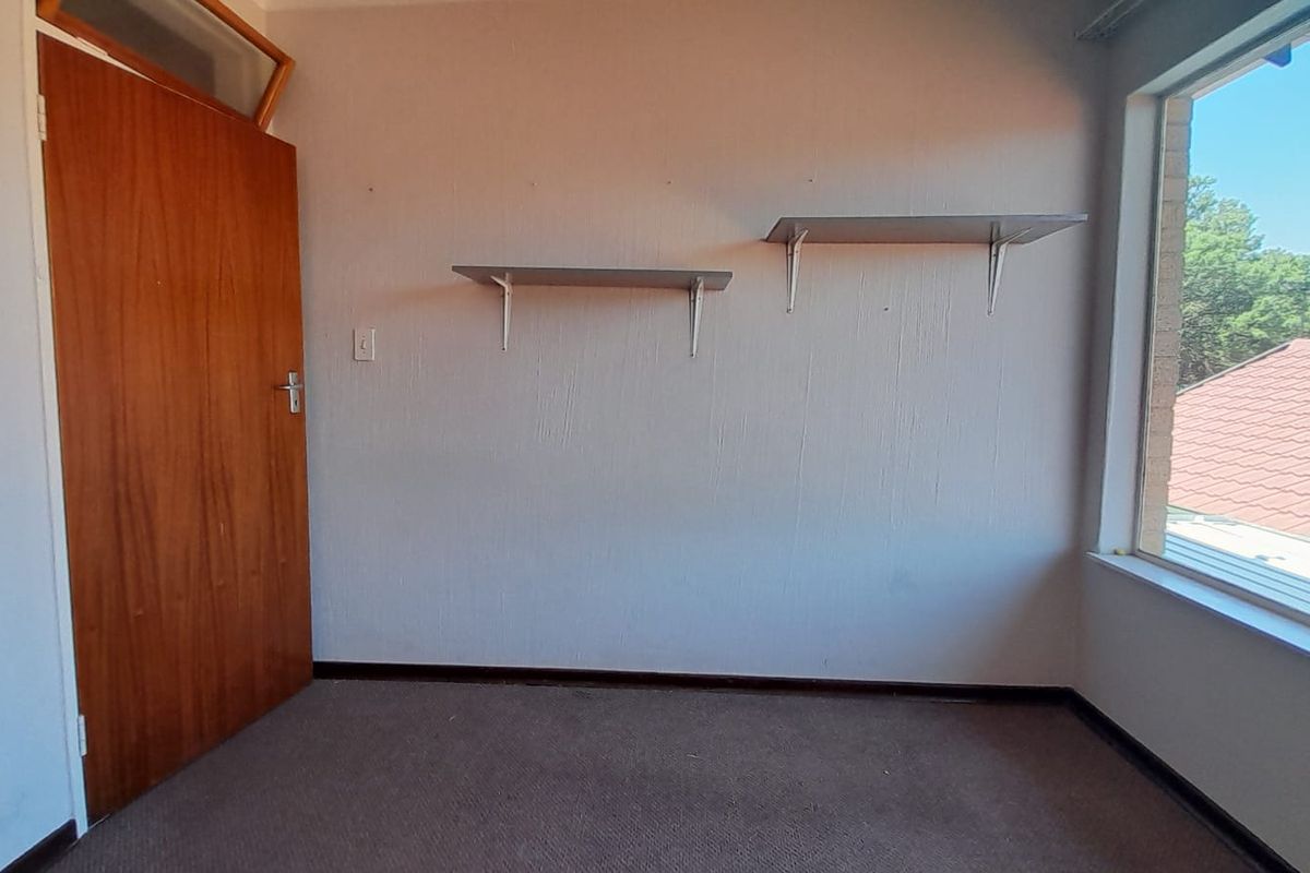 An empty bedroom featuring a wooden door, wall-mounted shelving, and a large window with natural light, ready for renovation or staging.