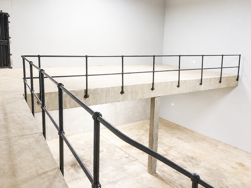 Industrial utility space featuring a concrete mezzanine level with black metal safety railings and a secure exit door.
