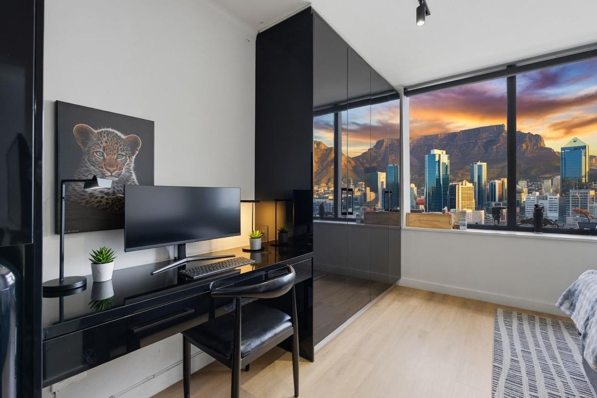 Modern bedroom featuring sleek built-in black cabinetry, light laminate flooring, and expansive windows offering a stunning city and mountain view.