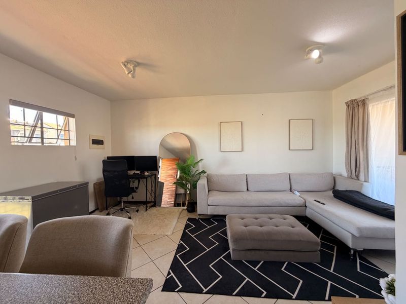 A spacious living room featuring tiled flooring, ceiling spotlights, and a sliding glass door providing natural light.