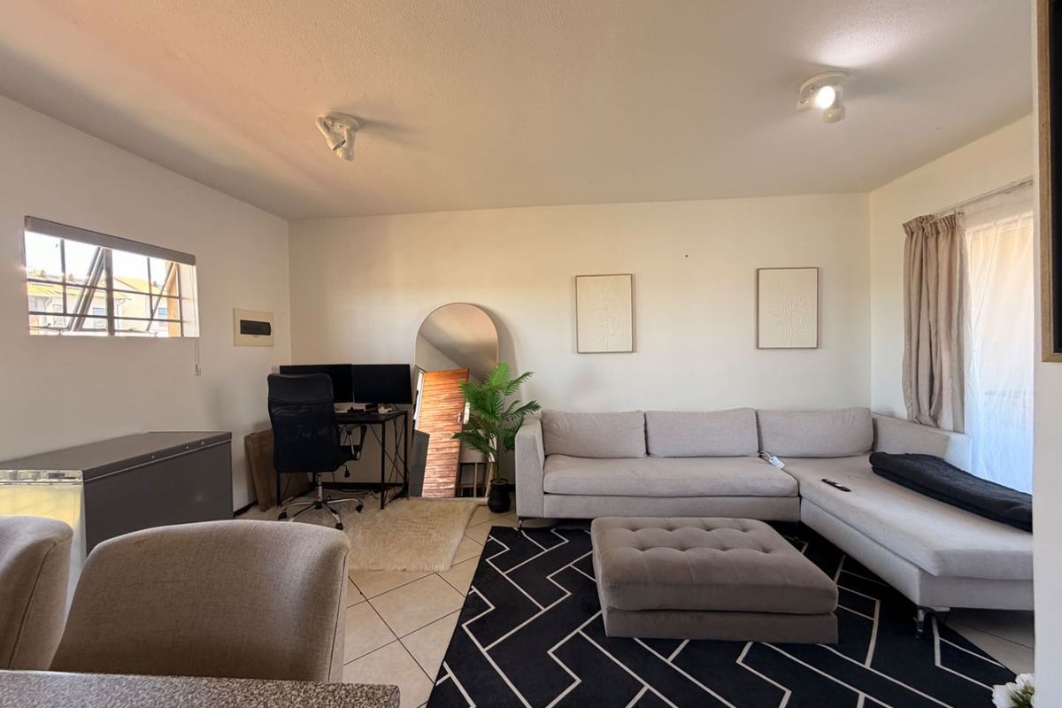 A spacious living room featuring tiled flooring, ceiling spotlights, and a sliding glass door providing natural light.