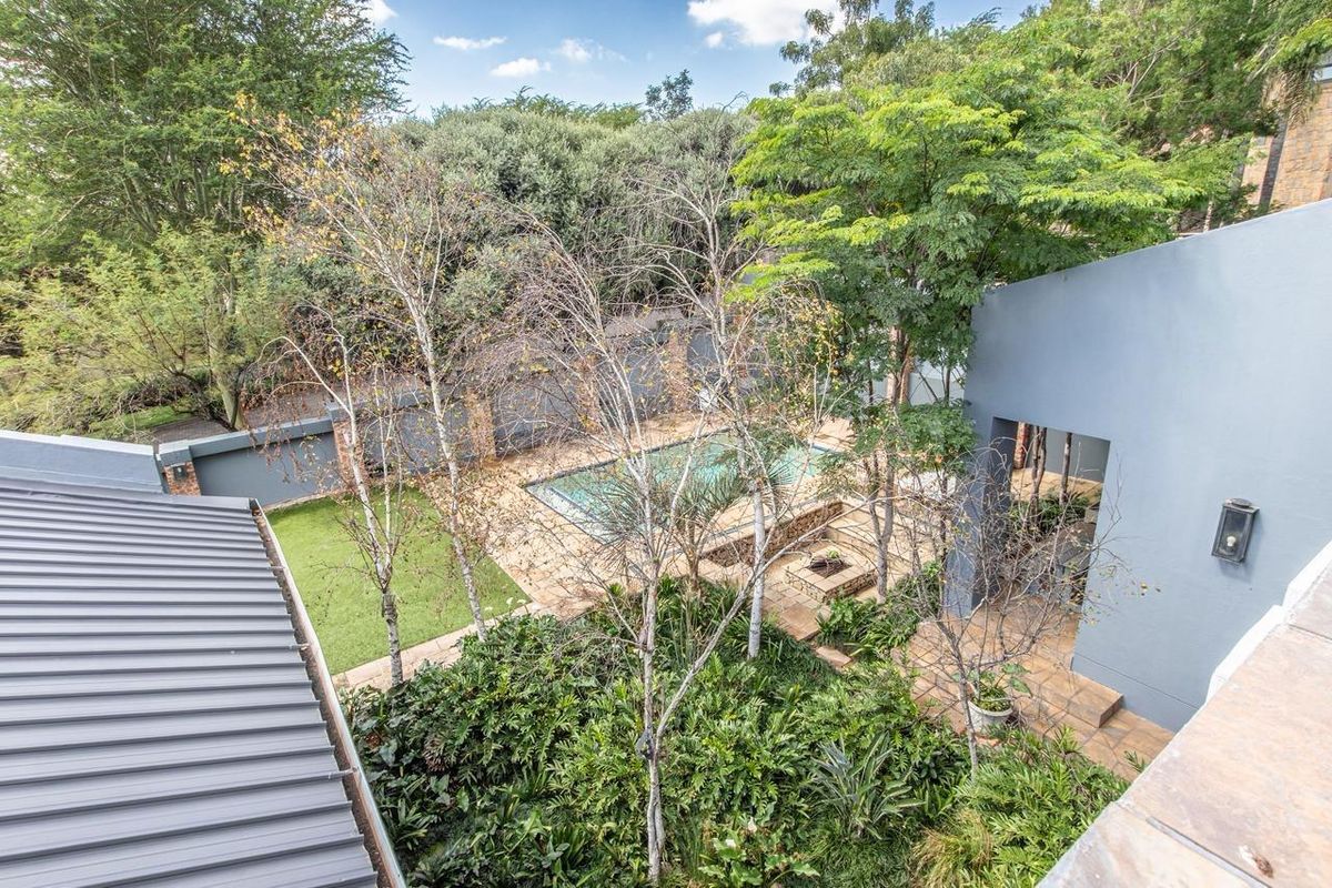 Aerial view of a private backyard featuring a swimming pool, stone-paved patio with a fire pit, and established garden landscaping.