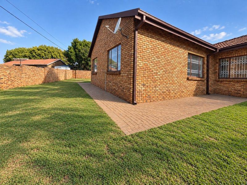 A view of the rear exterior featuring face brick walls, a paved patio area, and a well-maintained lawn enclosed by a brick boundary wall.